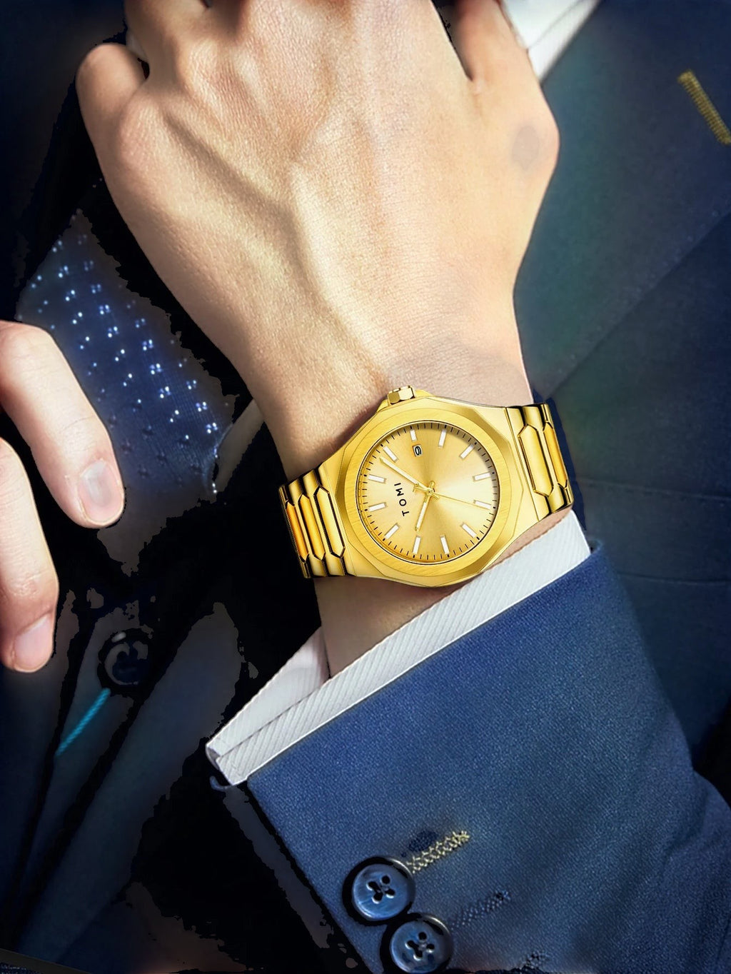My Store gold stainless steel TOMI luxury wristwatch worn on a man's wrist with a navy blue suit jacket.